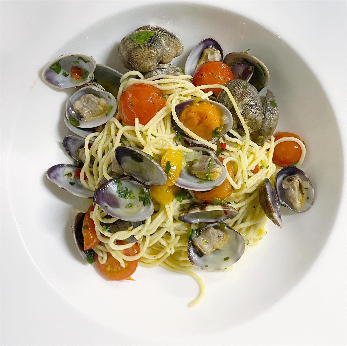 A white plate topped with spaghetti clams and tomatoes