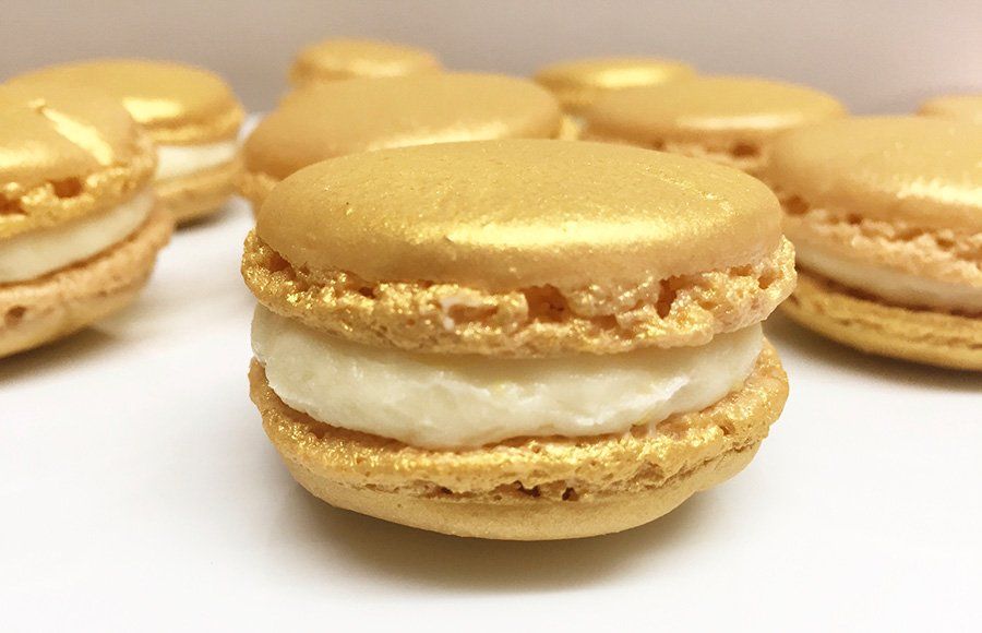 A close up of a gold macaroon with white frosting on a table.