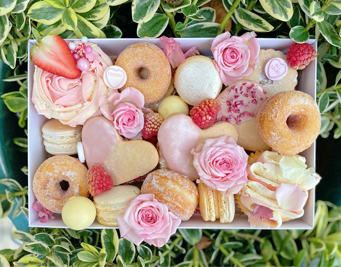 A box filled with a variety of desserts and flowers.