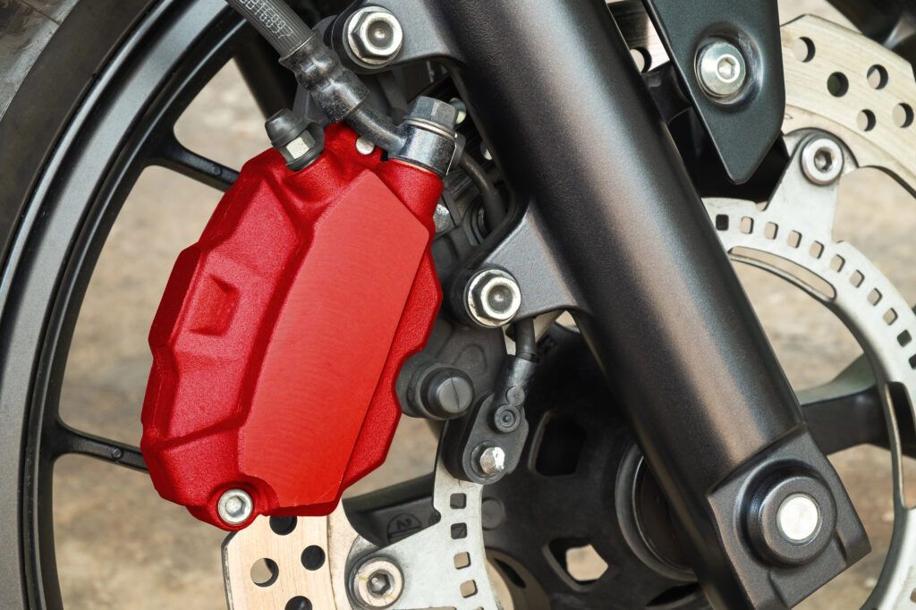 A bright red motorcycle brake caliper attached to the front wheel assembly of a bike.