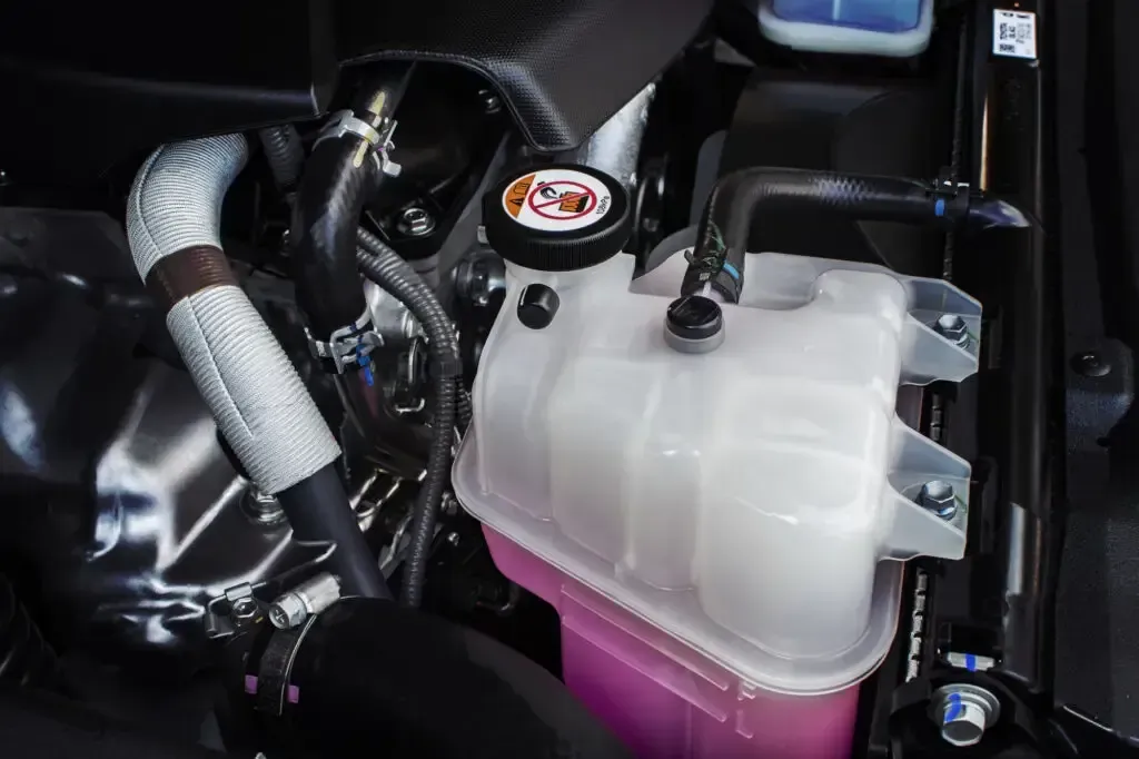 An engine bay showing a translucent coolant reservoir filled with pink liquid and a radiator cap.