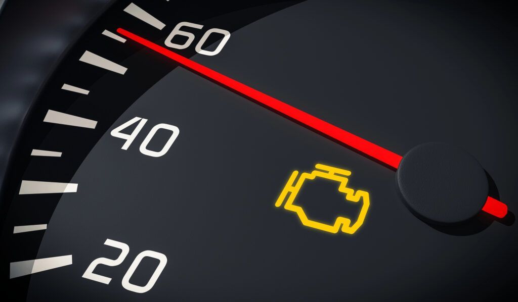 A yellow check engine light illuminated on a dark car dashboard with a speedometer needle pointing past 60.