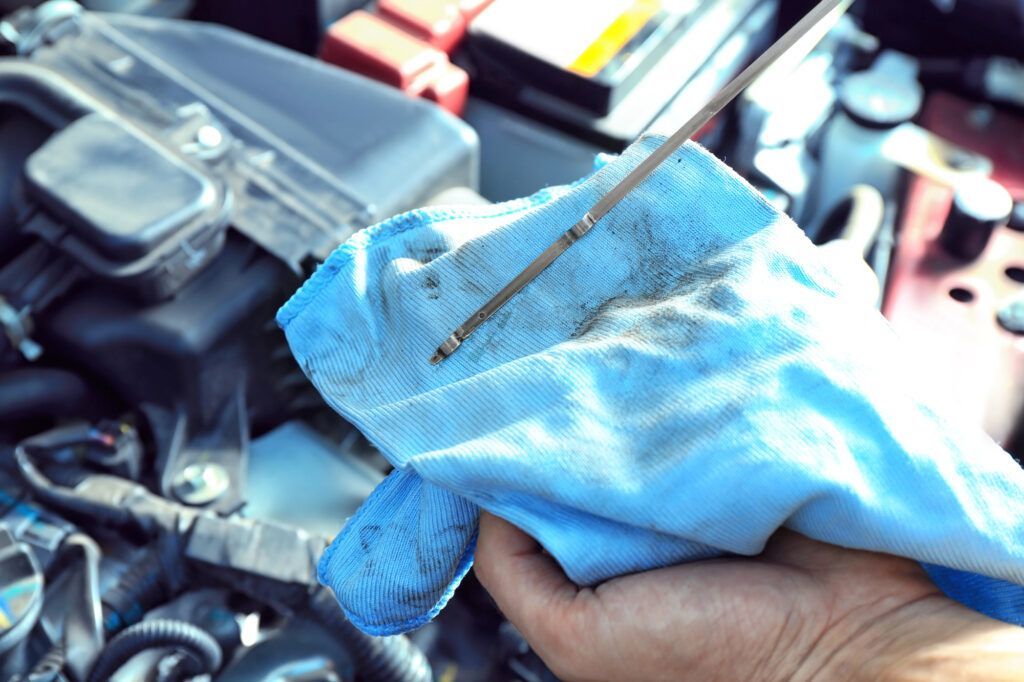 A hand holds a car engine oil dipstick against a blue cloth to check the oil level in an engine bay.