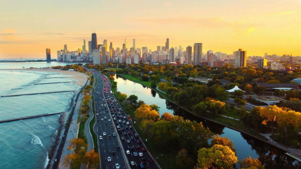 Aerial view of Chicago's skyline at sunset, featuring Lake Shore Drive traffic next to Lake Michigan and Lincoln Park.