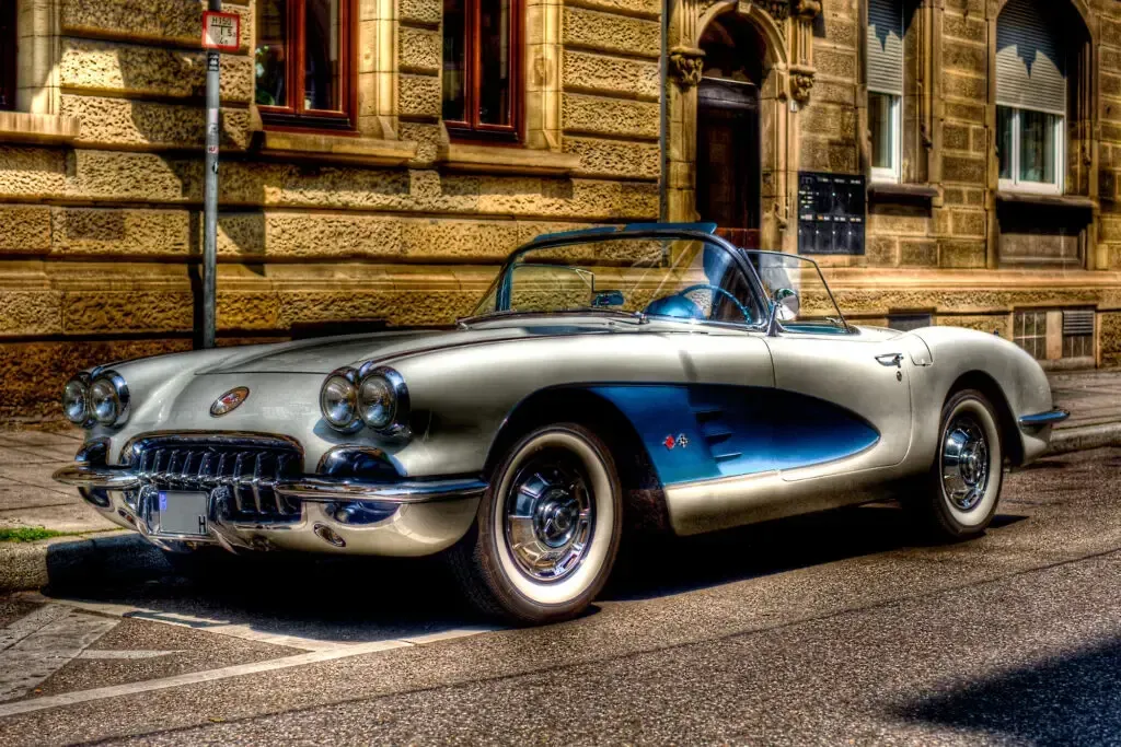 A silver and blue vintage convertible parked on a city street in front of a stone building.