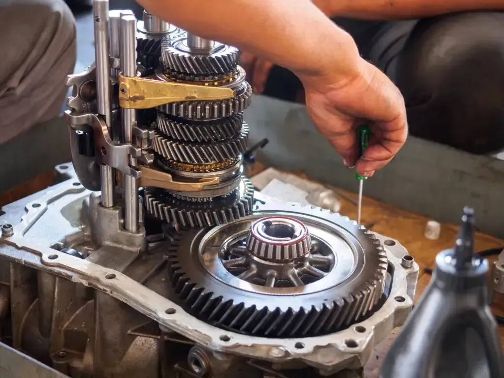 A mechanic uses a screwdriver to work on the internal gears of an open automotive transmission system.