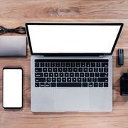 Laptop, smartphone, and other electronics on a wooden desk.