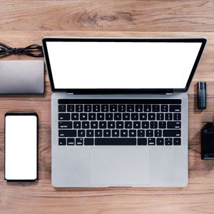 Laptop, smartphone, and other electronics on a wooden desk.