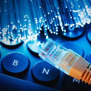 Ethernet cable on keyboard, fiber optic cables in background, blue lighting.