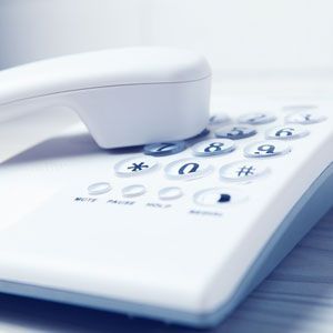 White landline phone, receiver off-hook, resting on the keypad with numbers and function buttons.