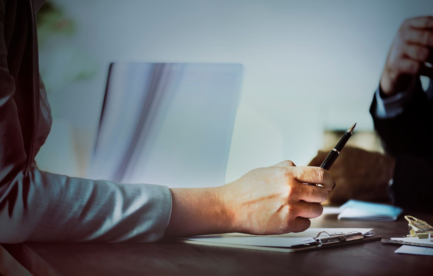 Hands signing a document across a desk in a meeting room