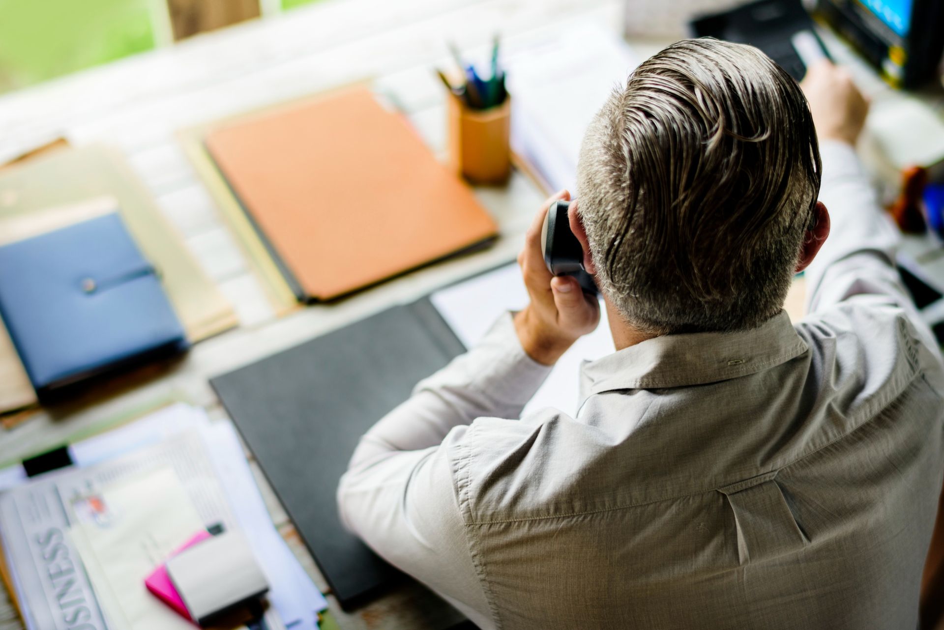 Person at a desk using a phone, surrounded by folders, papers, and office supplies.