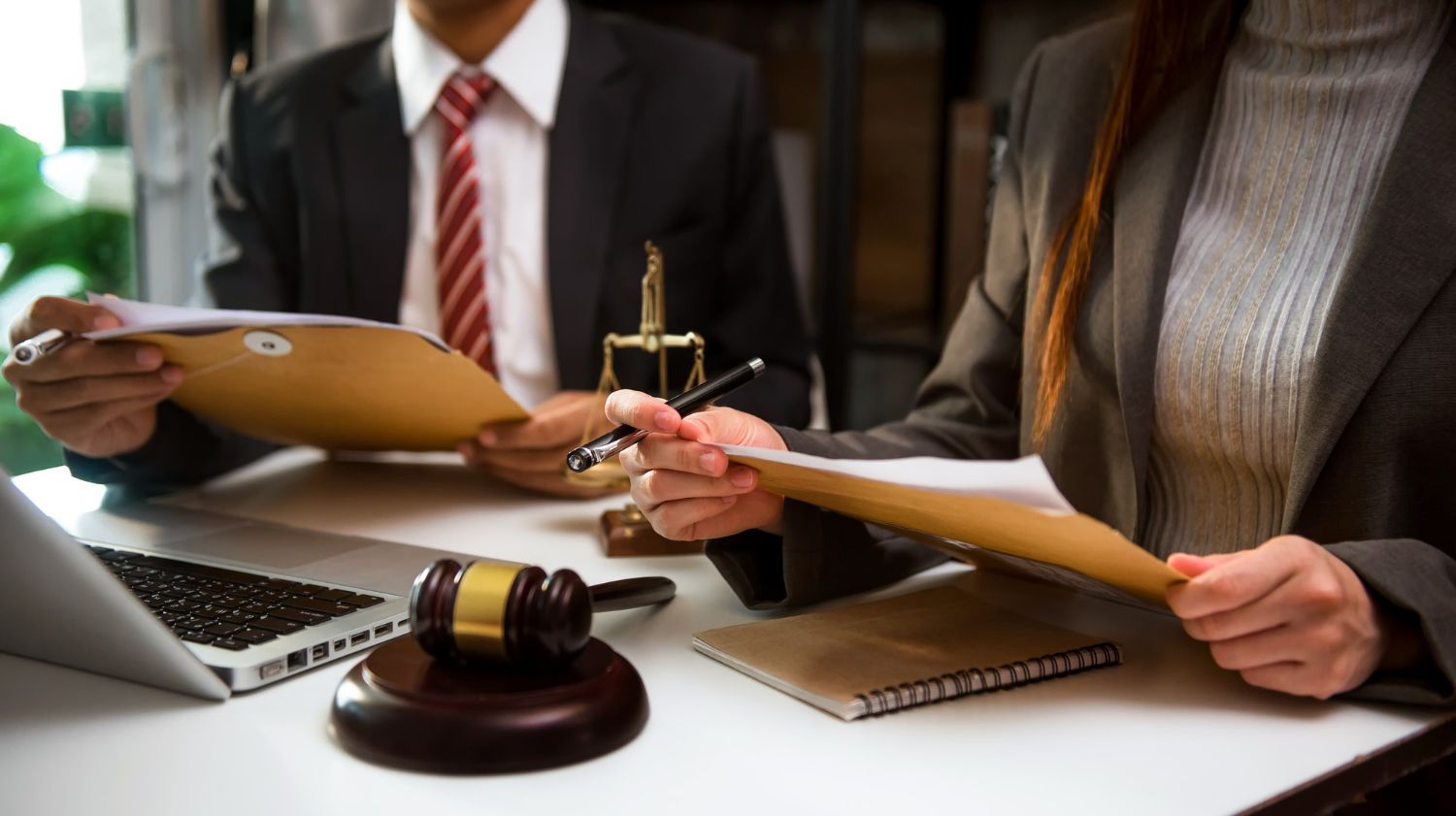 Two businesspeople reviewing documents at a desk with a laptop and judge’s gavel in a law office