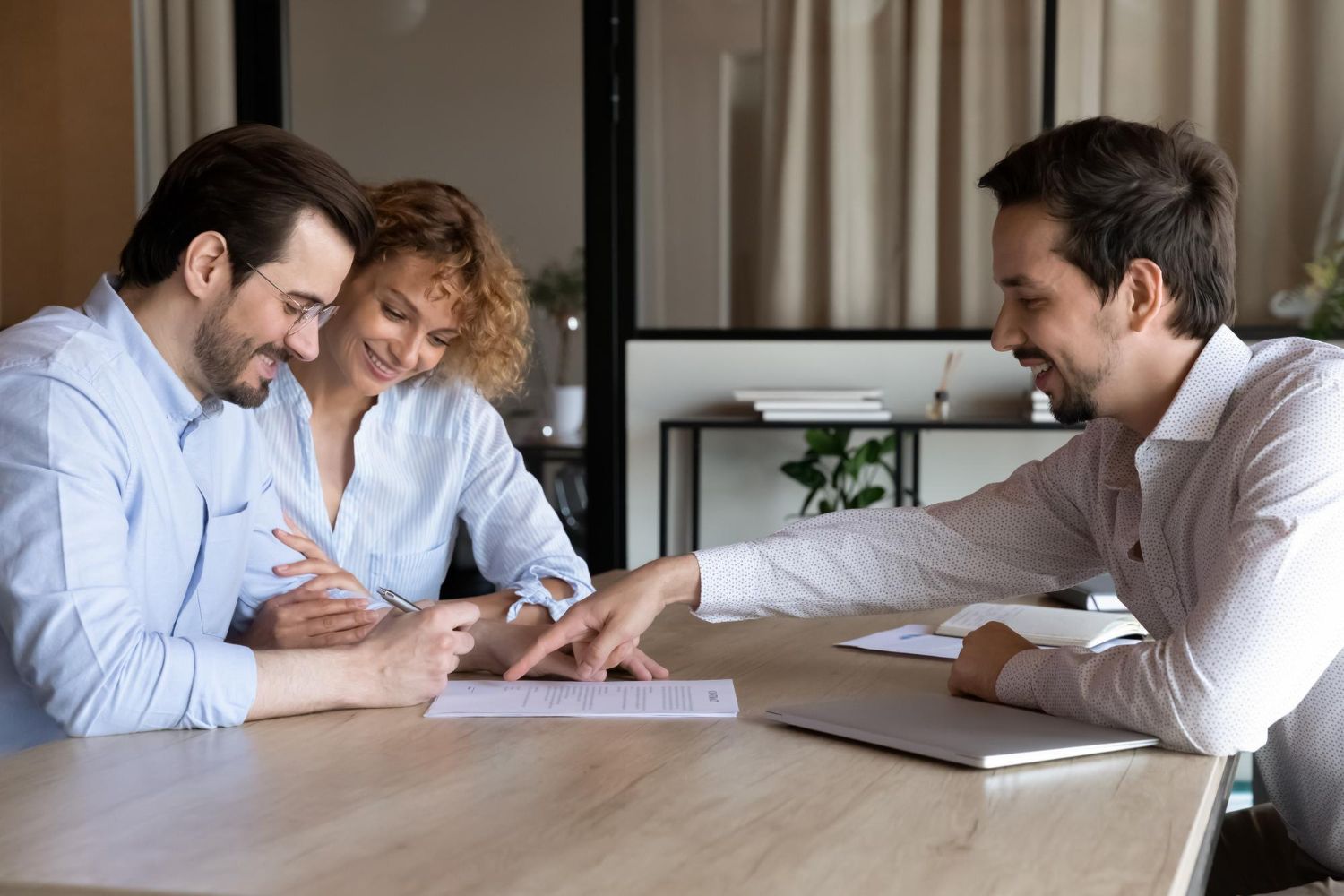 Three people in a meeting reviewing papers at a table in a bright office