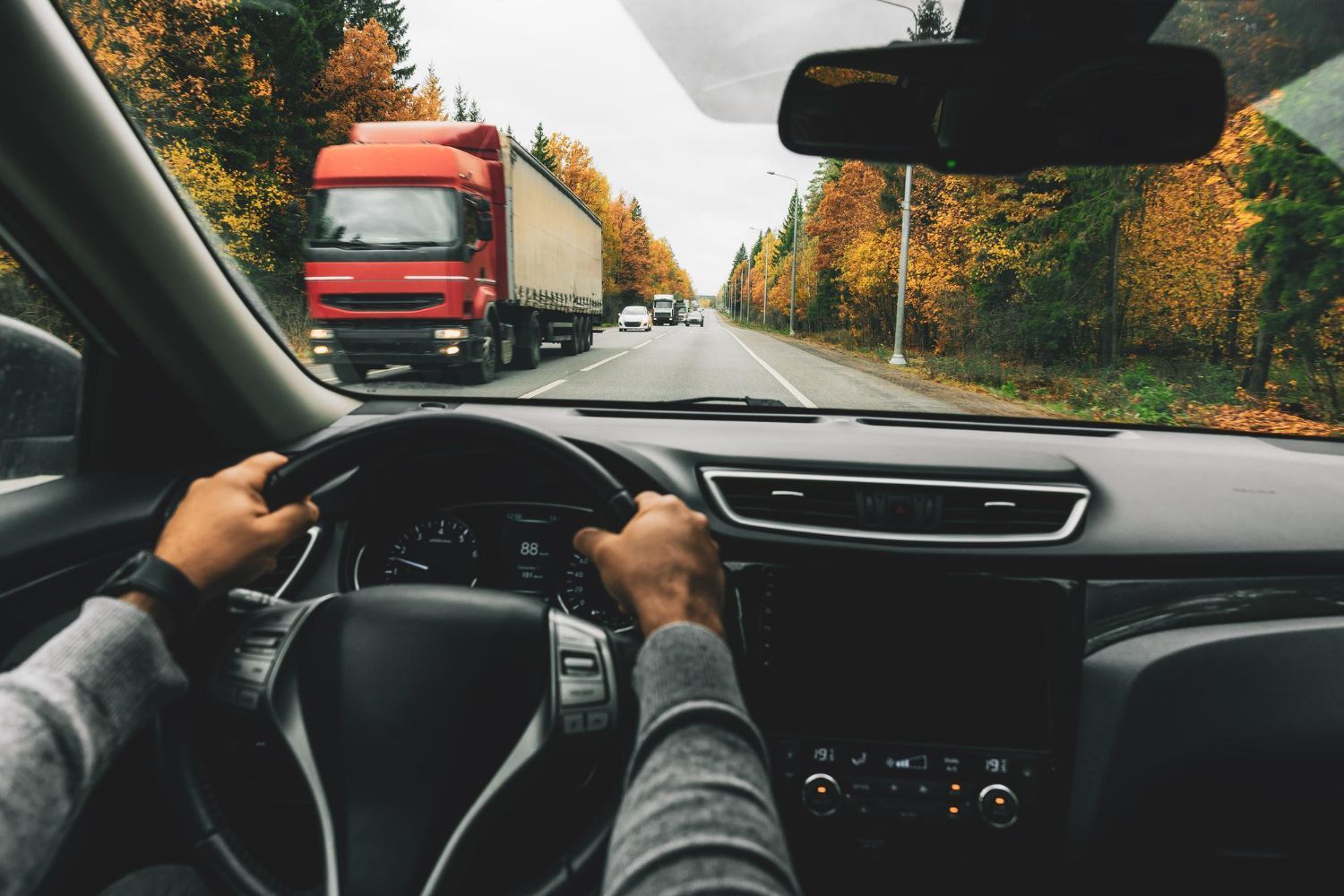 Driver’s view of a car on a highway, following a red truck past autumn trees