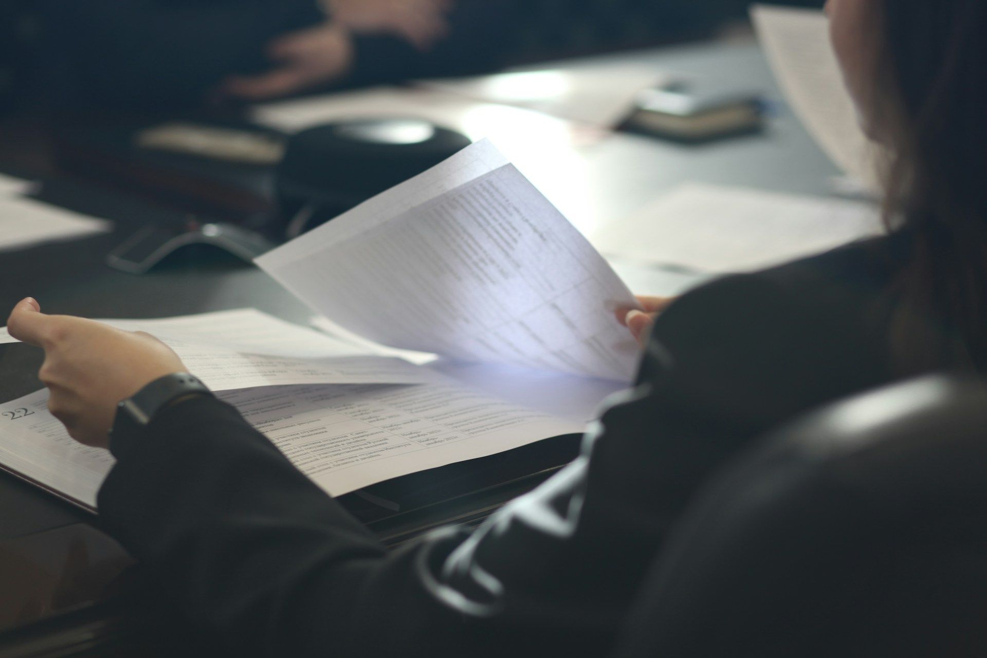 Person reading papers at a desk in a dim office, holding a sheet over an open notebook.