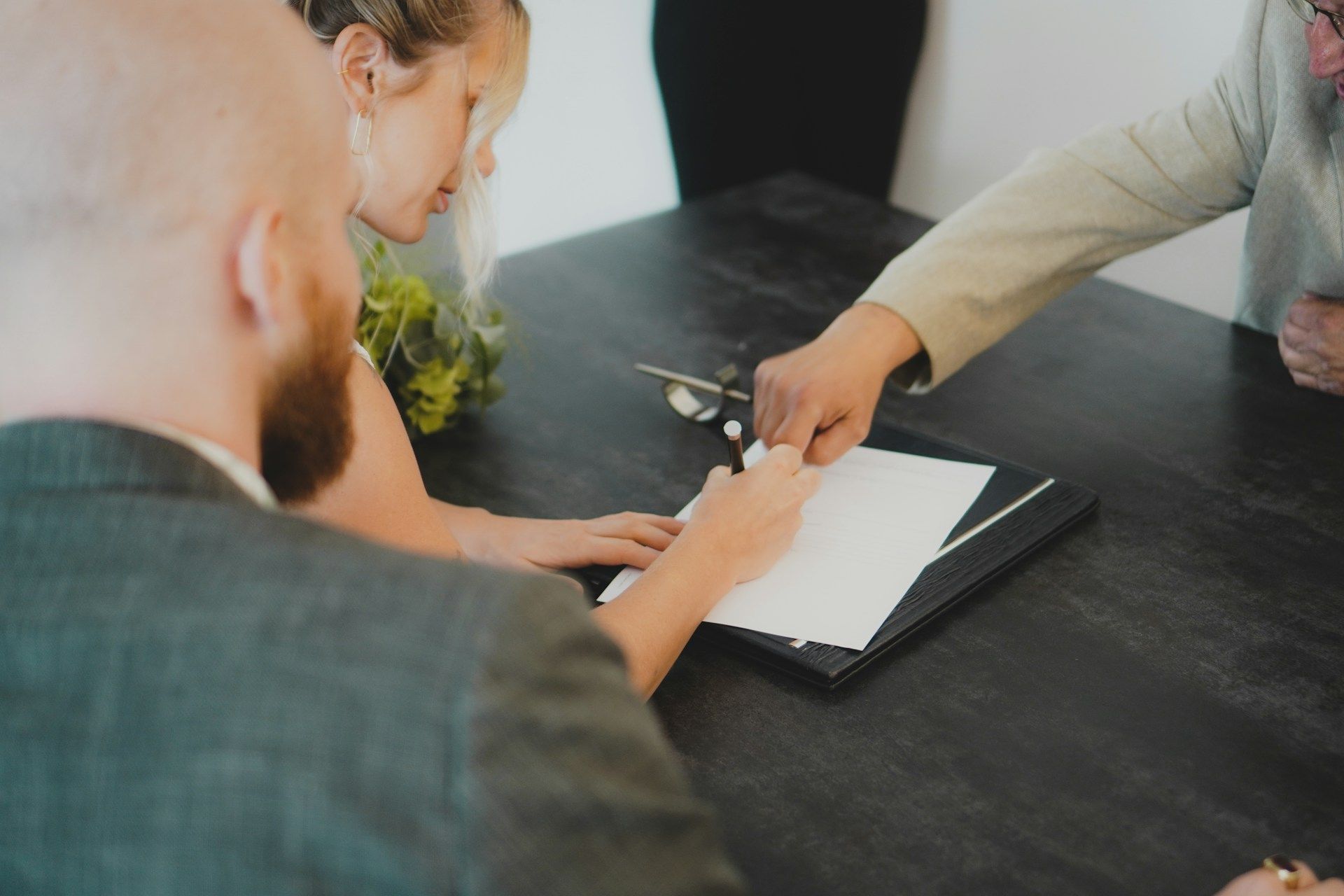 Two people signing a document at a dark table, with one pointing to the paper.