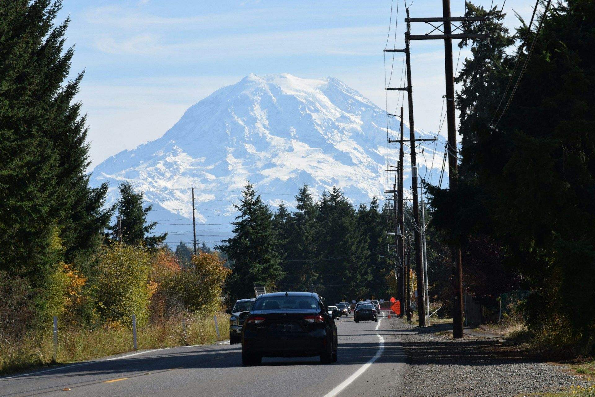 Cars on a tree-lined road with a snow-covered mountain in the distance.