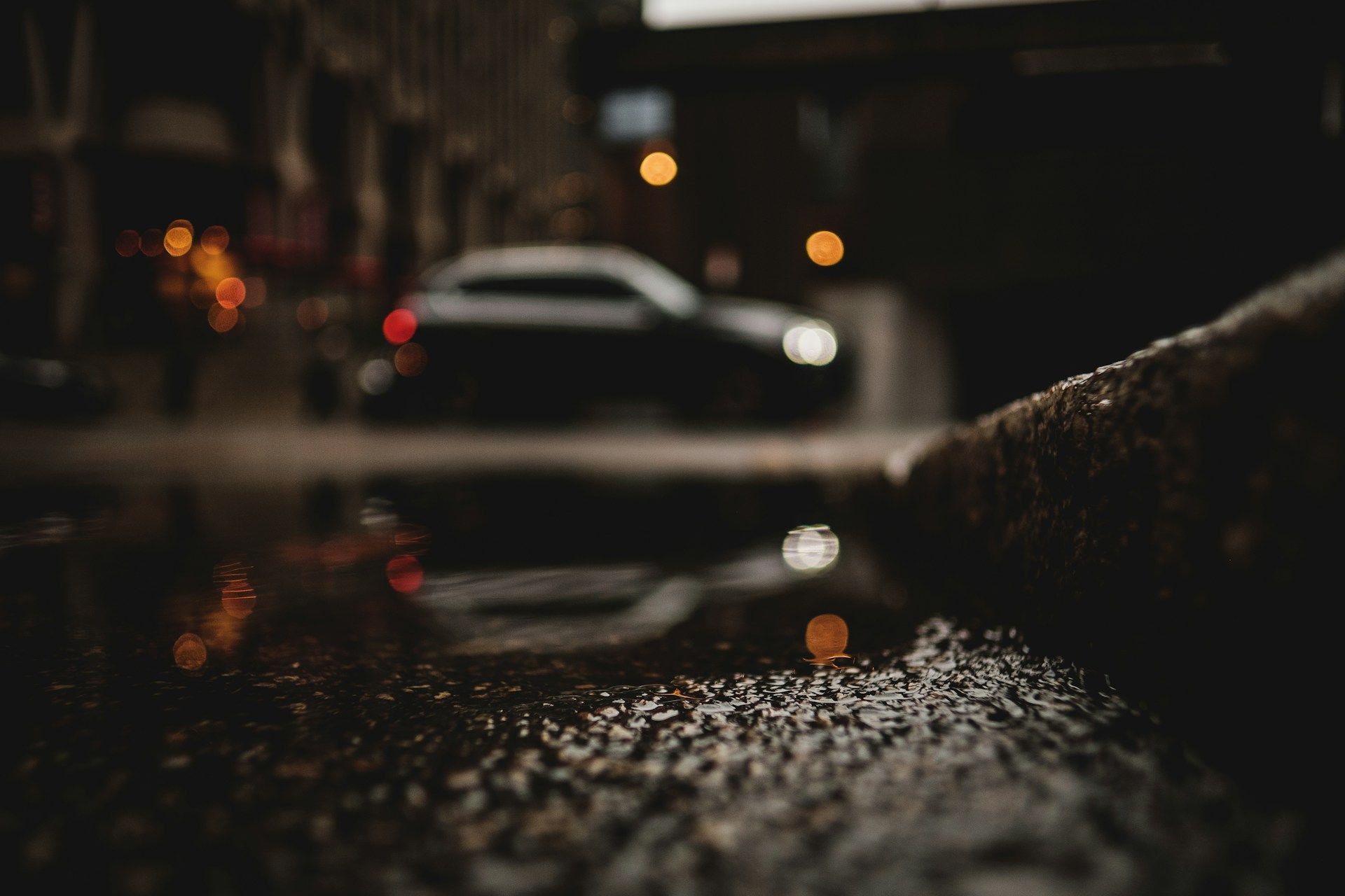 Blurred white car on a rainy street at night, with wet pavement reflecting lights