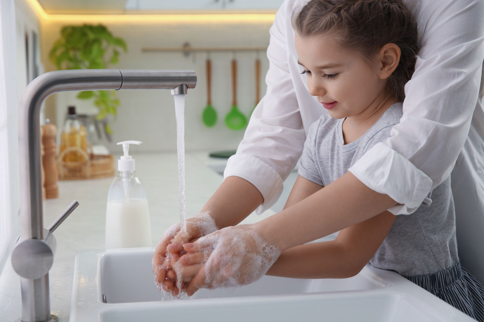 A woman and a little girl are washing their hands in a kitchen sink.