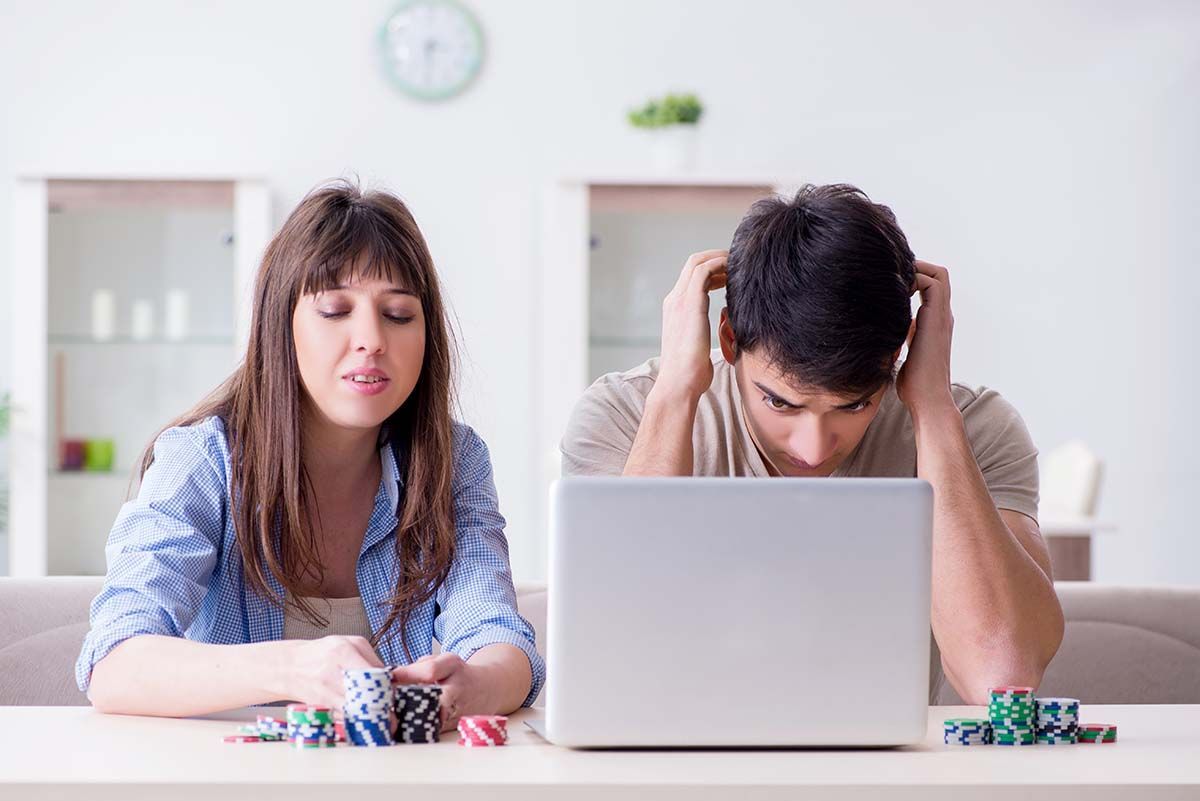 Two stressed people sitting at a table with a laptop and scattered dice, looking frustrated