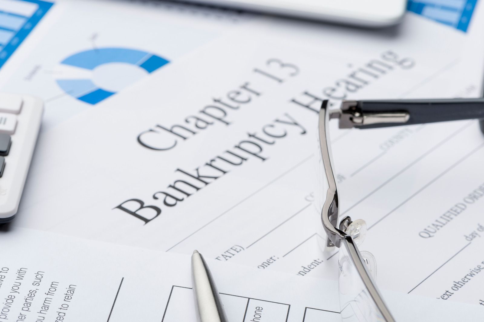 Bankruptcy documents on a desk with glasses and a calculator, showing “Chapter 13 Bankruptcy”