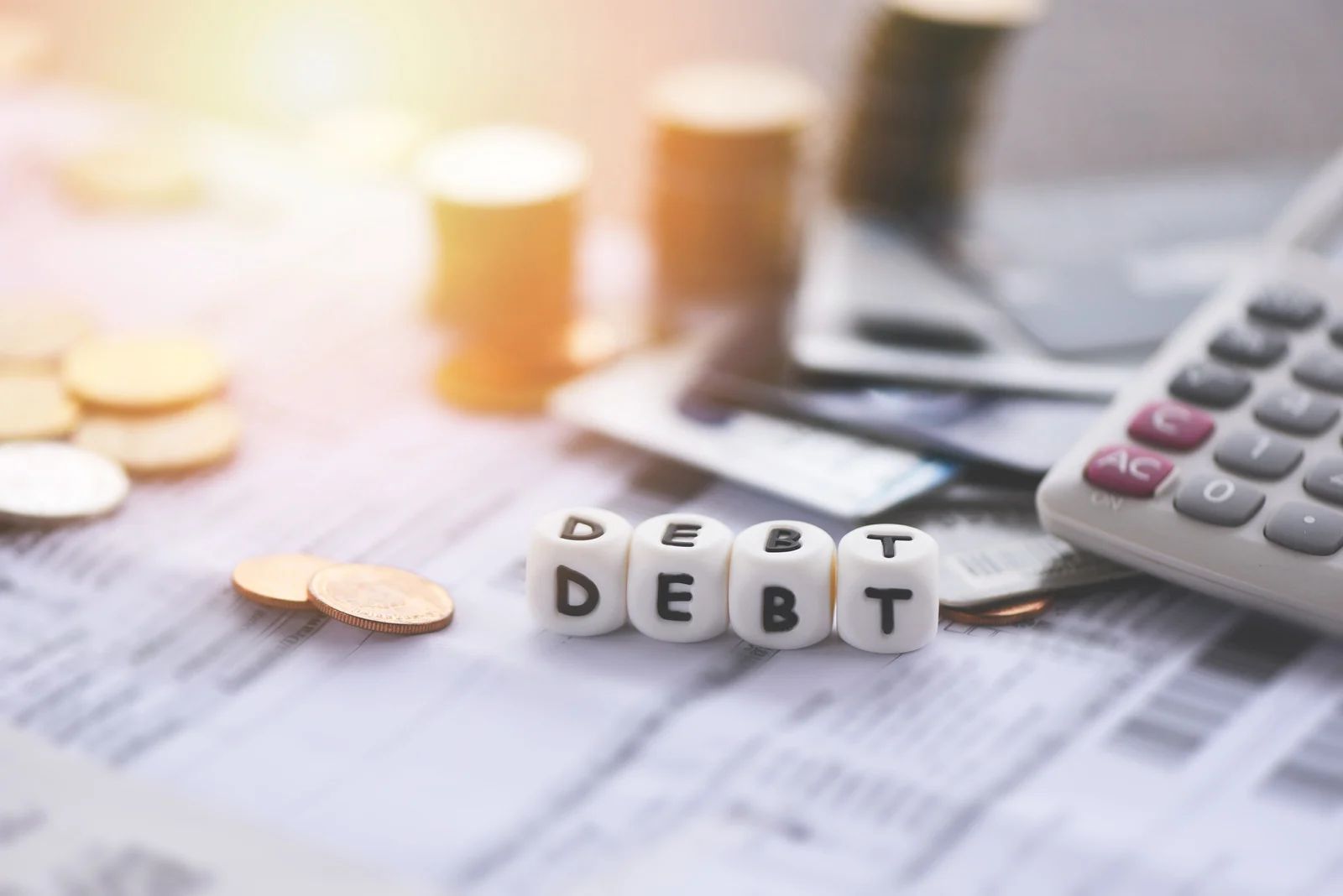 Coins, dice spelling “DEBT,” and a calculator on financial papers