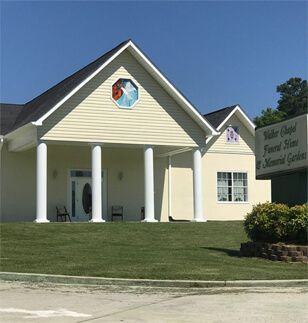 Yellow community center building with white columns and a sign beside a grassy lawn.