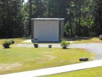 Small gray shed in a grassy yard beside a curved driveway, with trees in the background.
