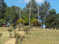 Grassy park hillside with trees, large cross monuments, and a few people in the background