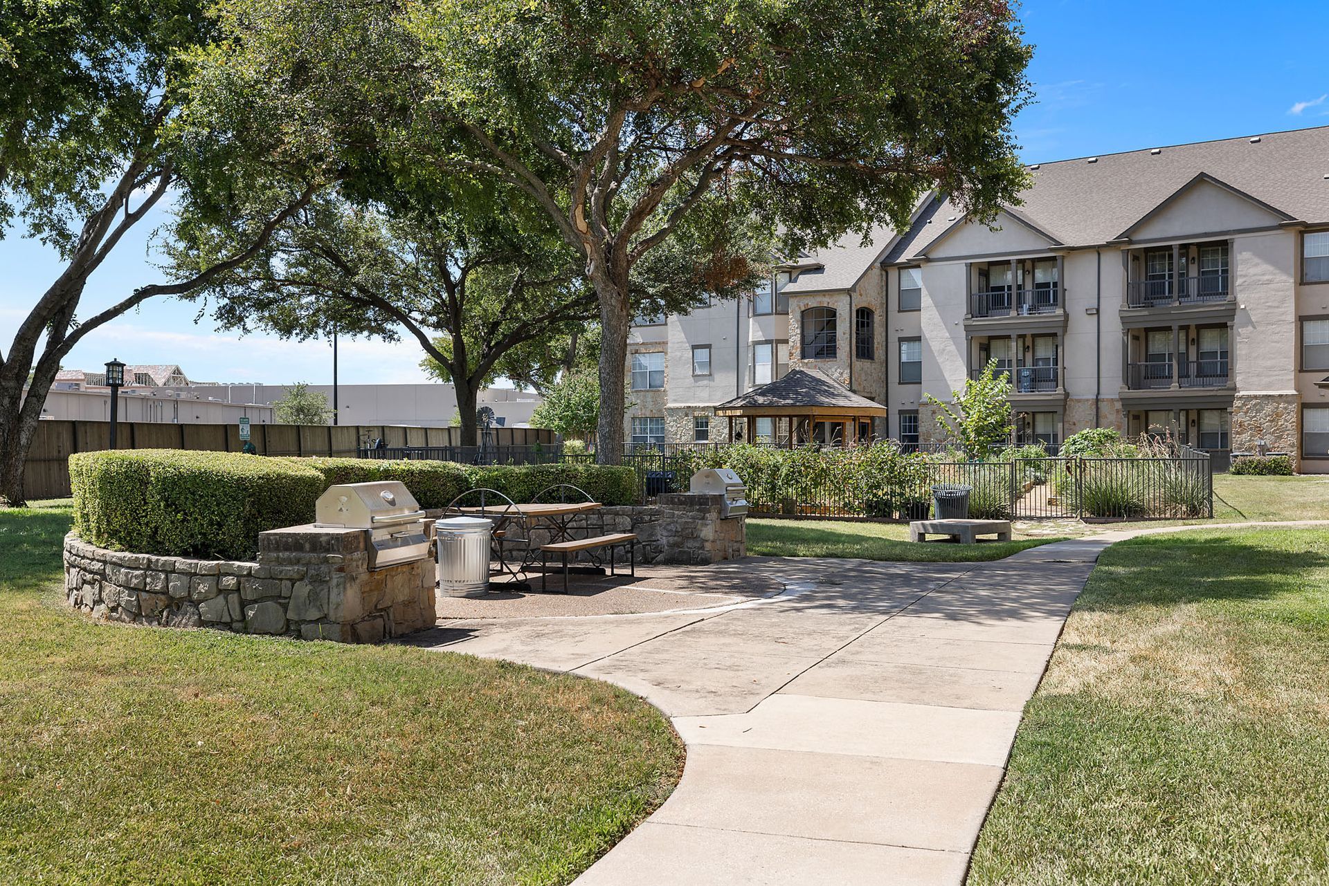 Apartment courtyard with tree, stone seating wall, and paved walkway in front of balconies at Marquis at Bellaire Ranch in Fort Worth, TX