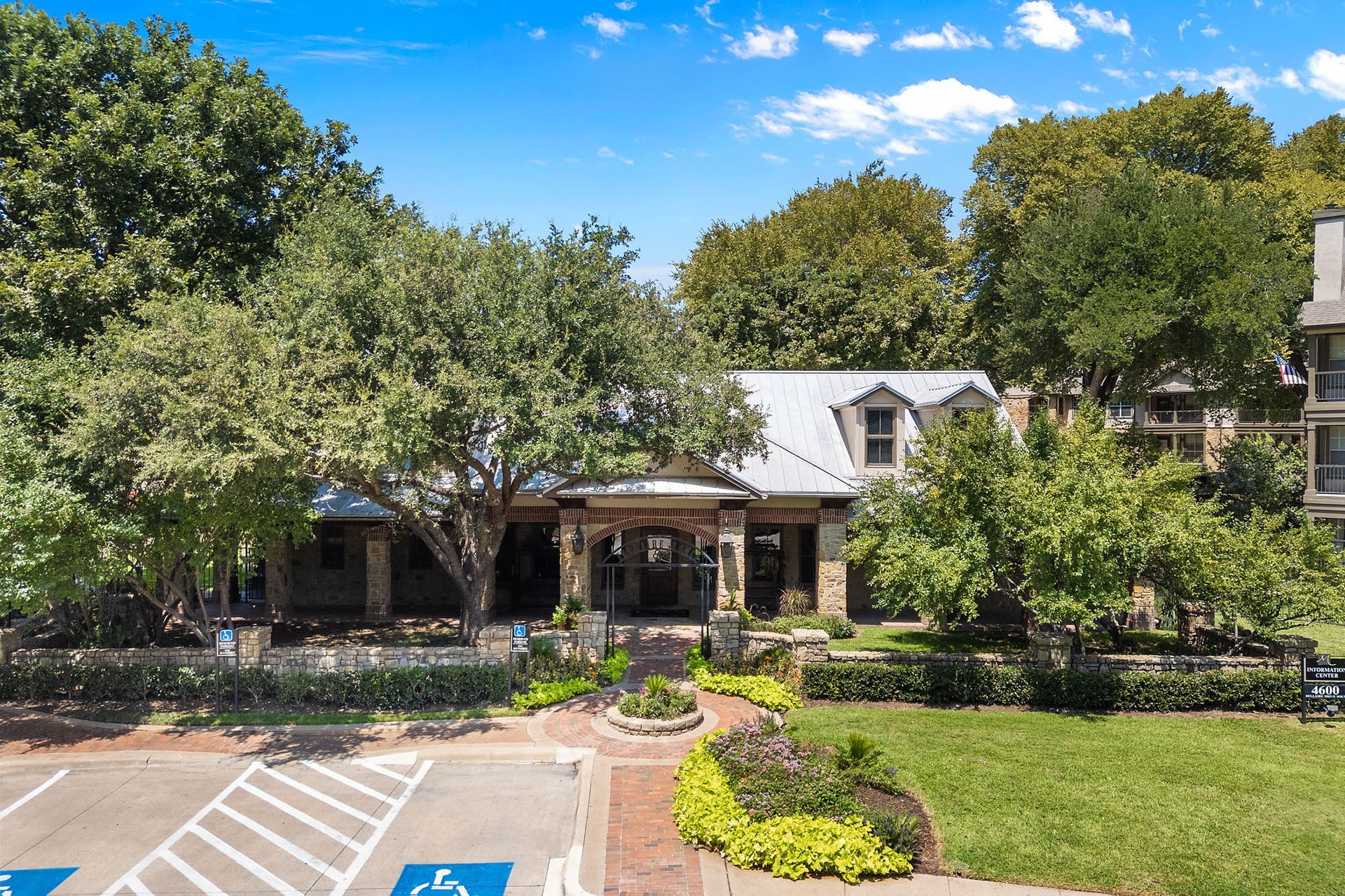 Apartment building entrance with trees, landscaped garden, and parking spaces in front at Marquis at Bellaire Ranch in Fort Worth, TX