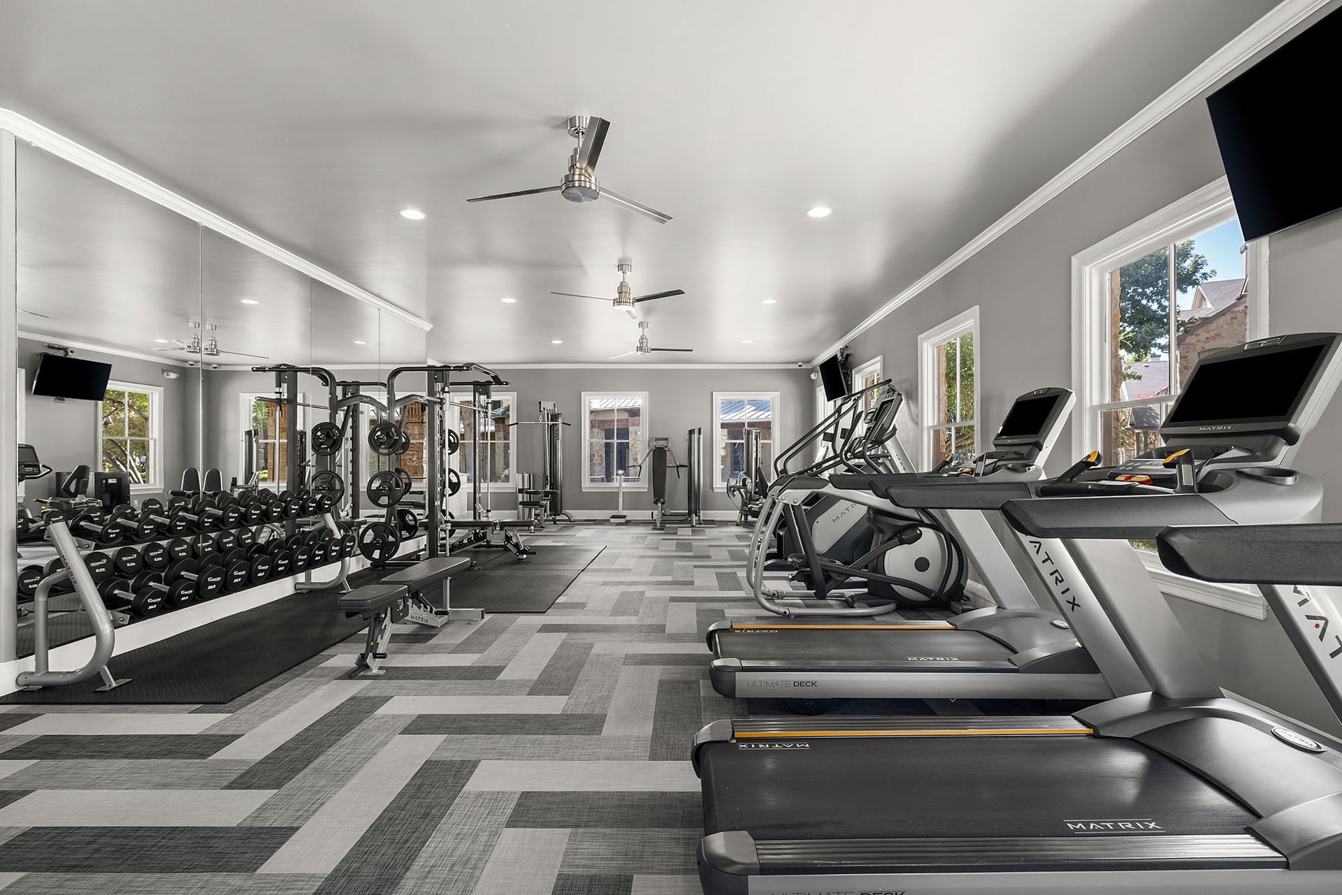 Bright modern gym with treadmills, dumbbells, and weight machines under recessed lighting at Marquis at Bellaire Ranch in Fort Worth, TX.