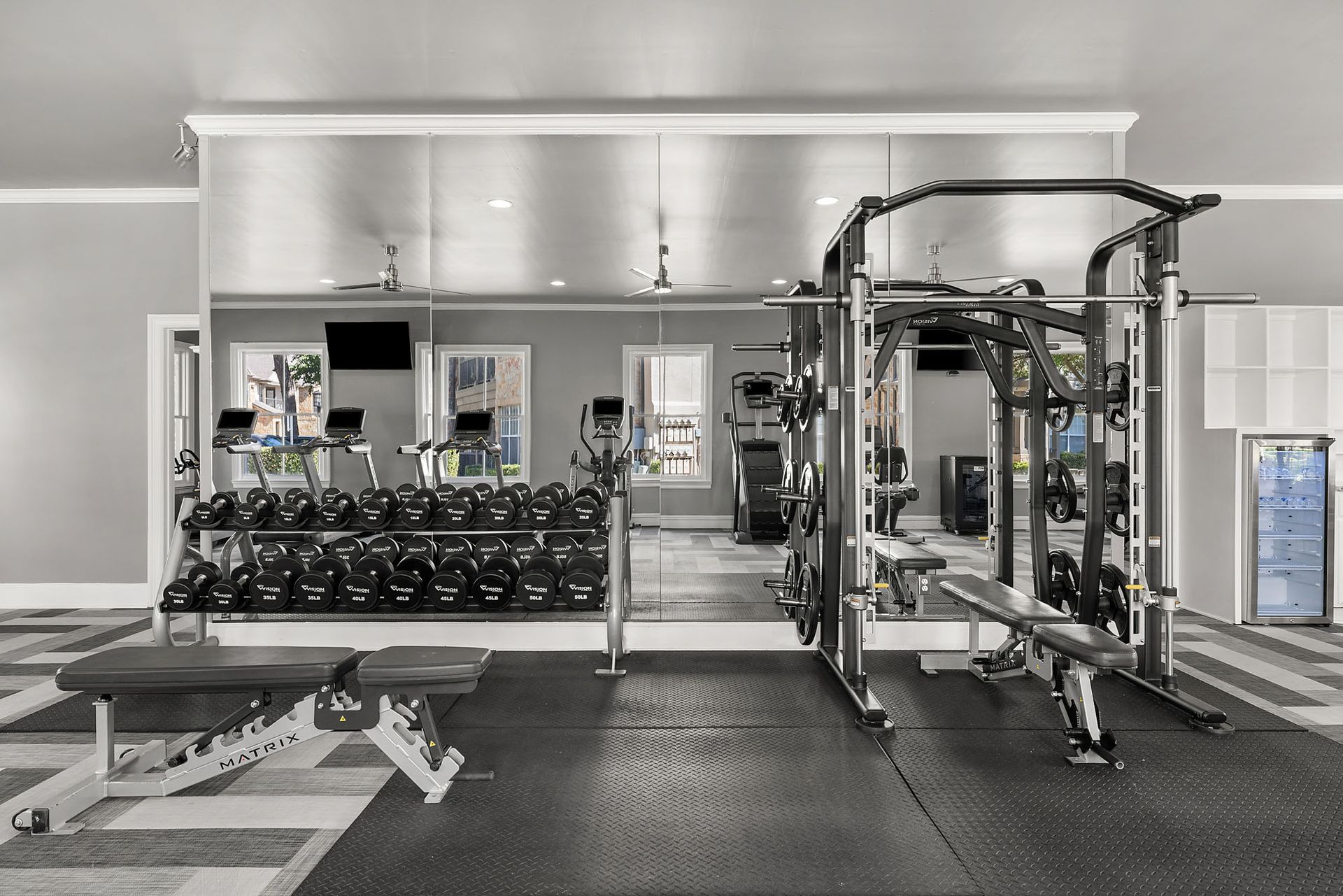 Modern gym interior with weight racks, cable machines, and a bench against mirrored walls at Marquis at Bellaire Ranch in Fort Worth, TX.