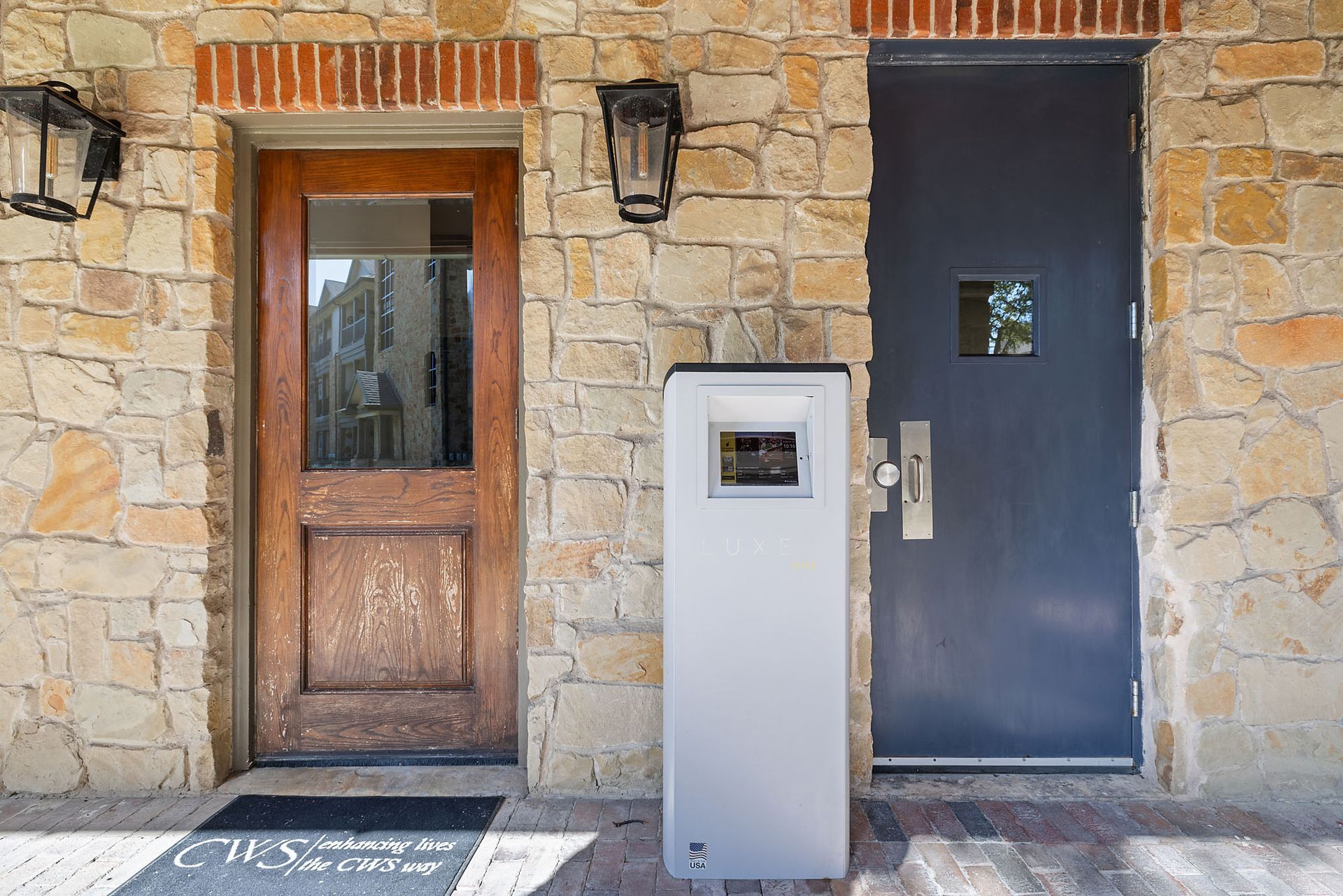 Stone building facade with a wooden door, black door, and gray intercom panel at Marquis at Bellaire Ranch in Fort Worth, TX.