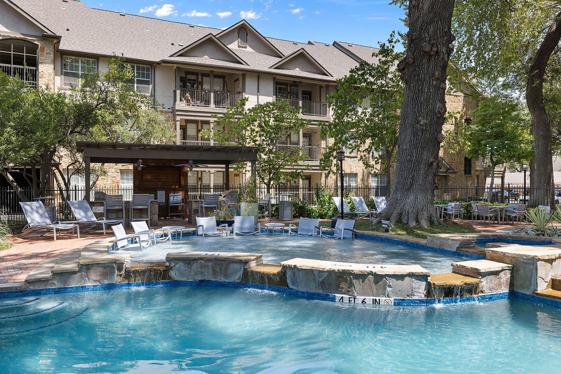 Resort-style outdoor pool with loungers, trees, and a lodge building in the background at Marquis at Bellaire Ranch in Fort Worth, TX
