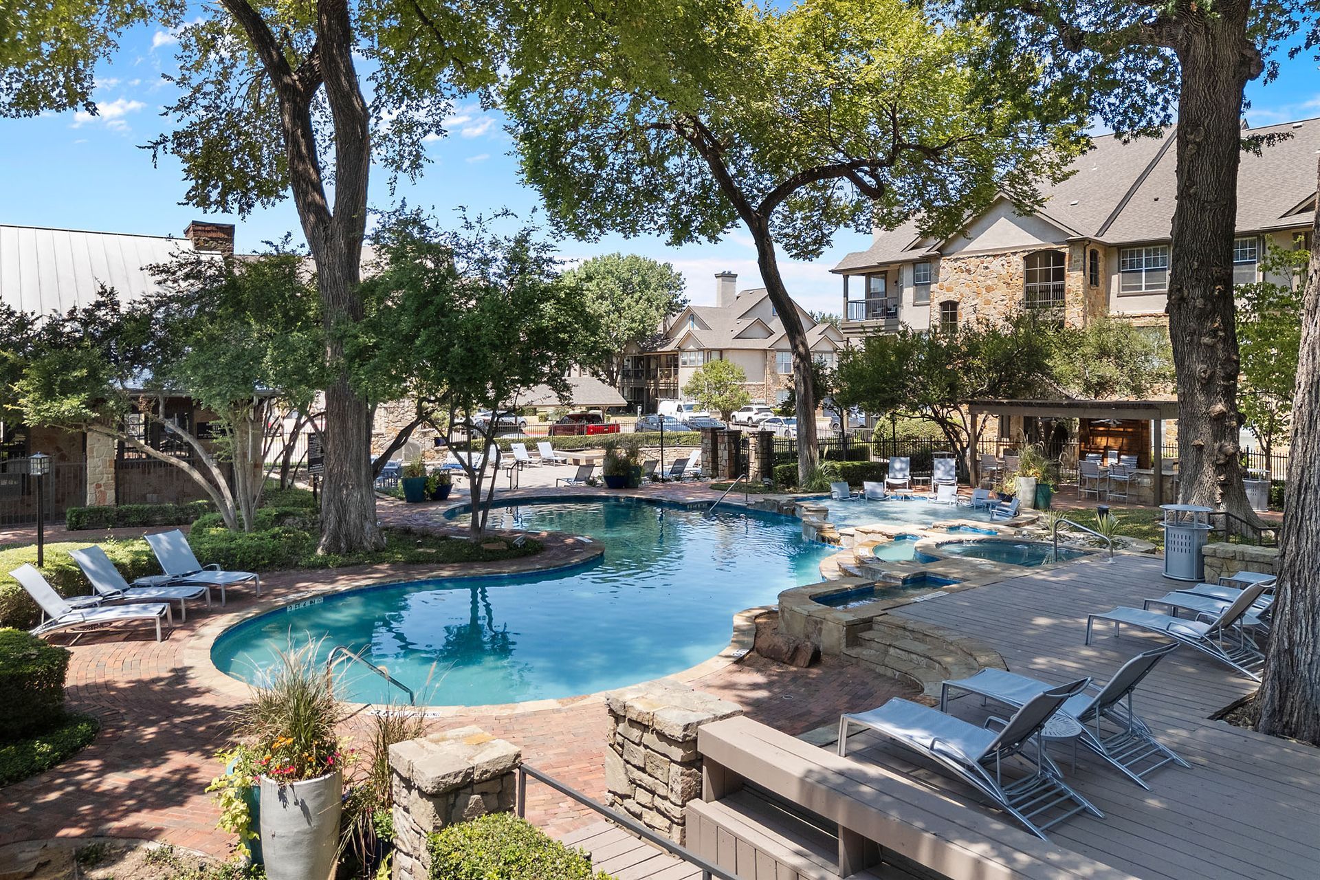 Resort pool with lounge chairs and trees in a sunny courtyard between apartment buildings at Marquis at Bellaire Ranch in Fort Worth, TX.