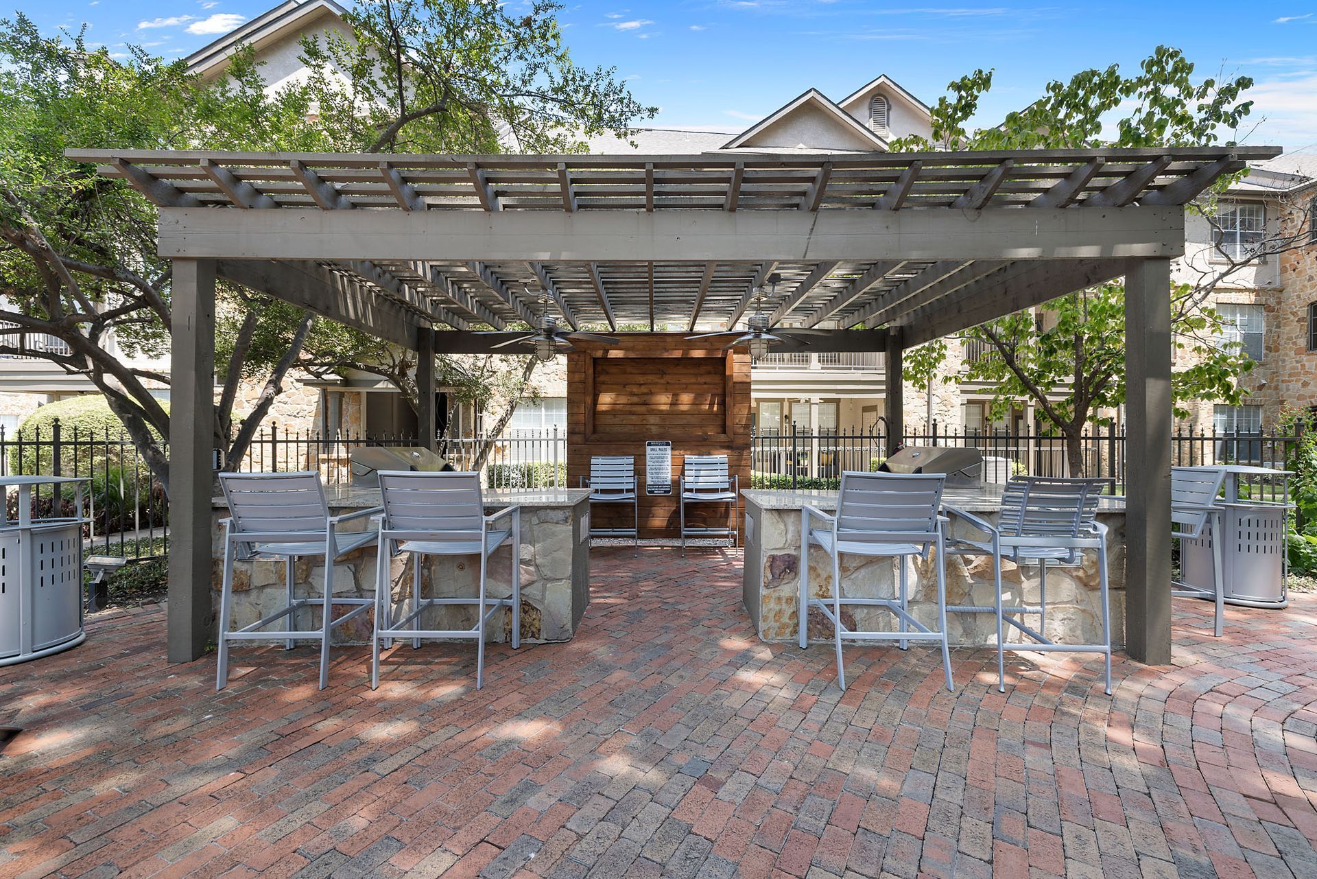 Outdoor brick patio with metal tables and chairs under a pergola in front of a building at Marquis at Bellaire Ranch in Fort Worth, TX