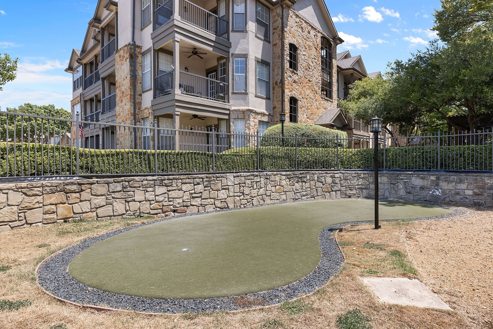 Outdoor fenced pet play area with artificial turf, stone border, and apartment building in the background at Marquis at Bellaire Ranch in Fort Worth, TX