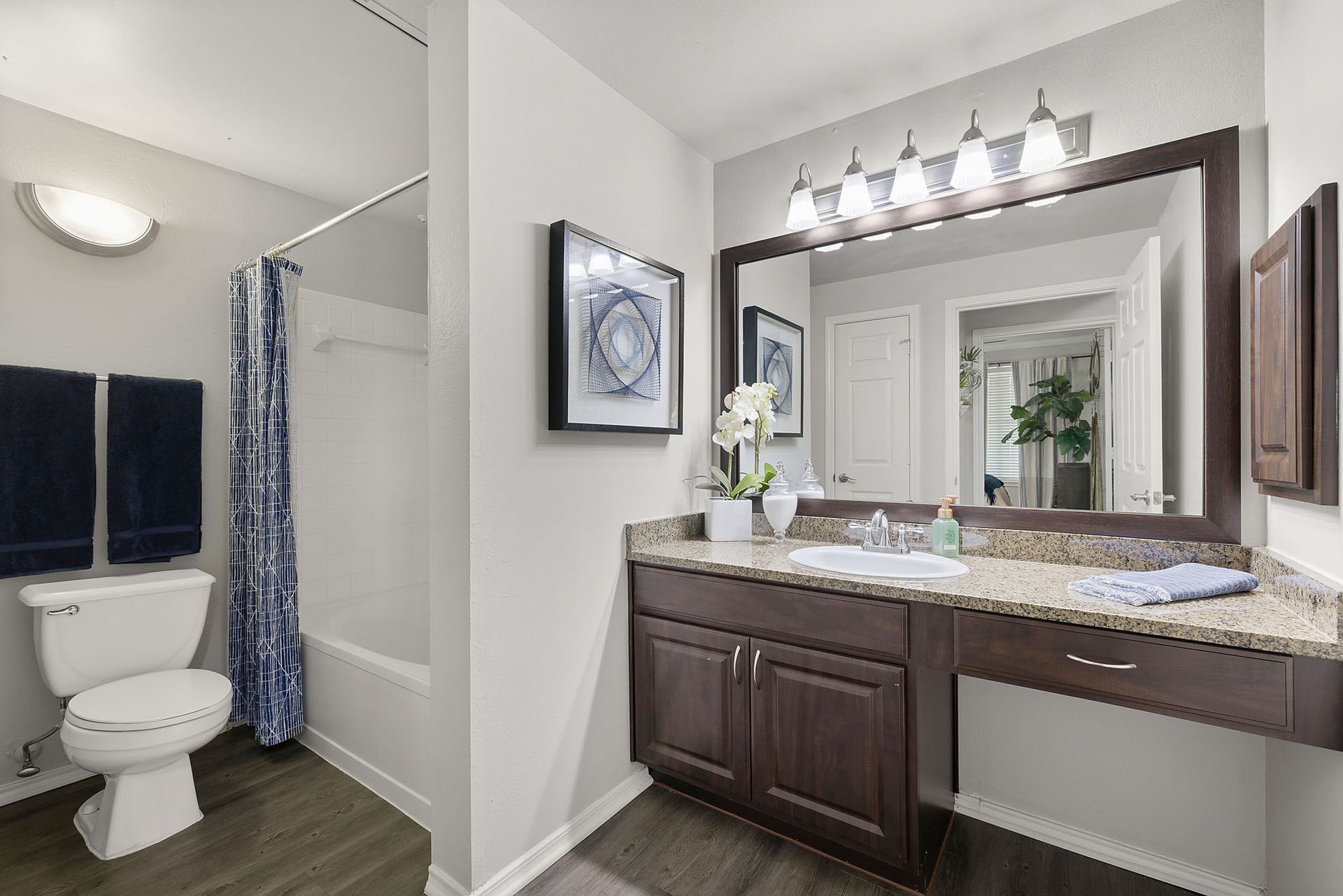 Bathroom with double vanity, large mirror, and shower-tub combo with blue curtain at Marquis at Bellaire Ranch in Fort Worth, TX