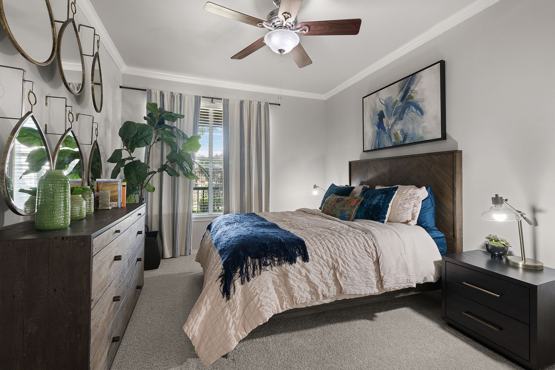 Bright bedroom with a bed, dresser, plants, and ceiling fan in neutral tones at Marquis at Bellaire Ranch in Fort Worth, TX