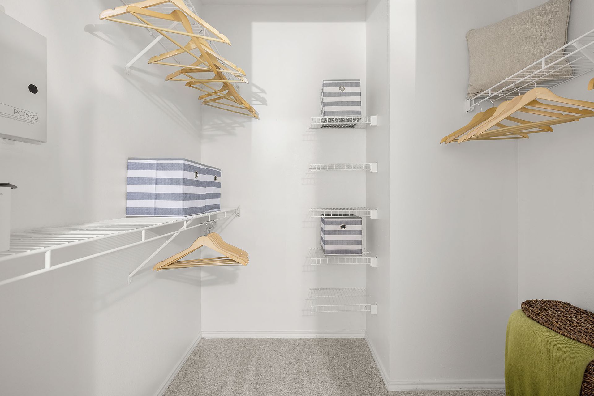 Walk-in closet with white shelves, hanging rods, striped storage boxes, and a green basket on the floor at Marquis at Bellaire Ranch in Fort Worth, TX