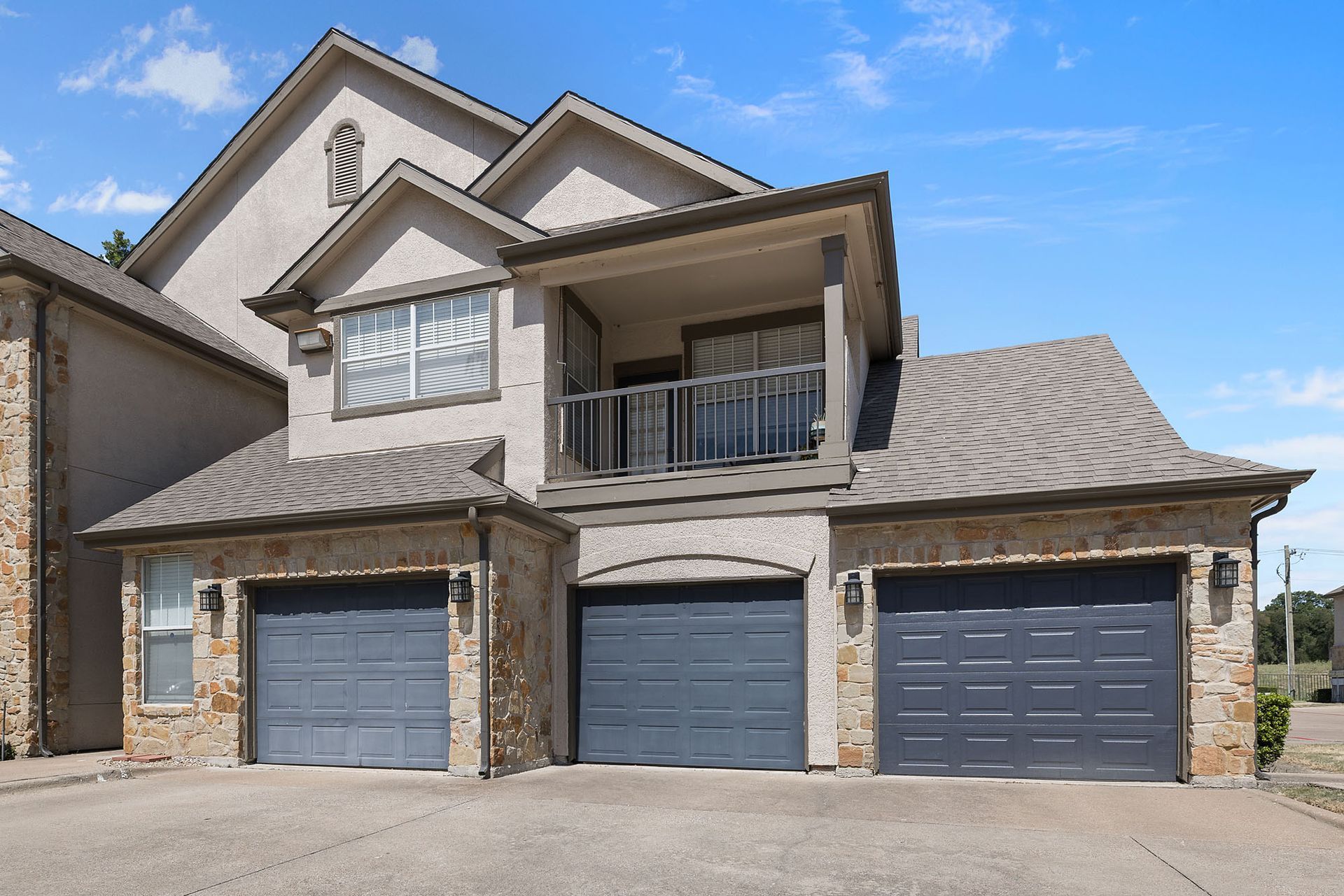 Three-story house with stone facade, balconies, and three garage doors under a clear blue sky at Marquis at Bellaire Ranch in Fort Worth, TX