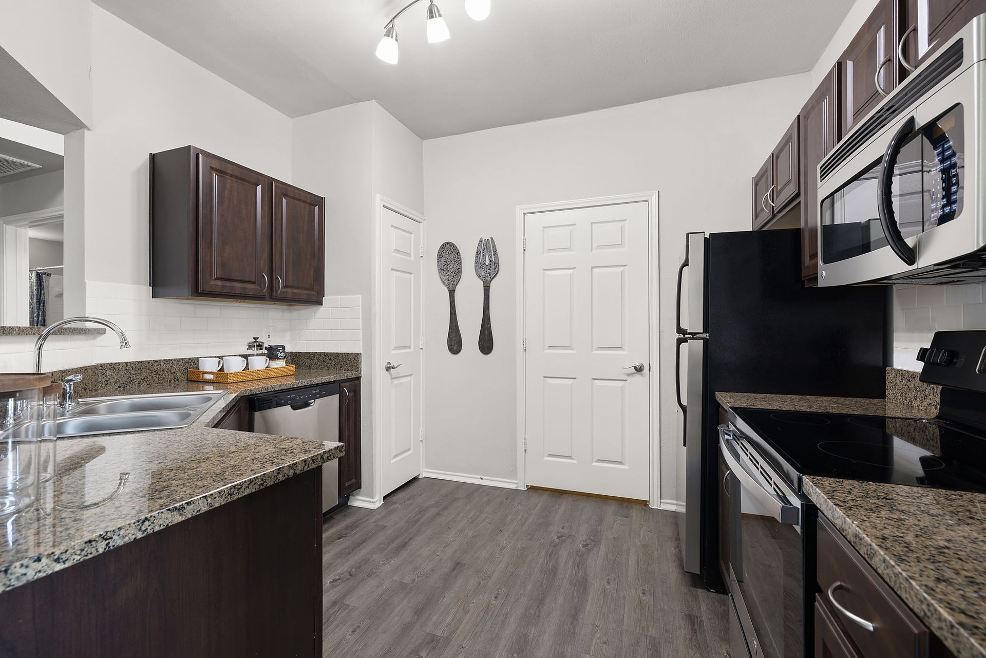 Modern kitchen with granite counters, dark cabinets, stainless appliances, and gray wood flooring at Marquis at Bellaire Ranch in Fort Worth, TX