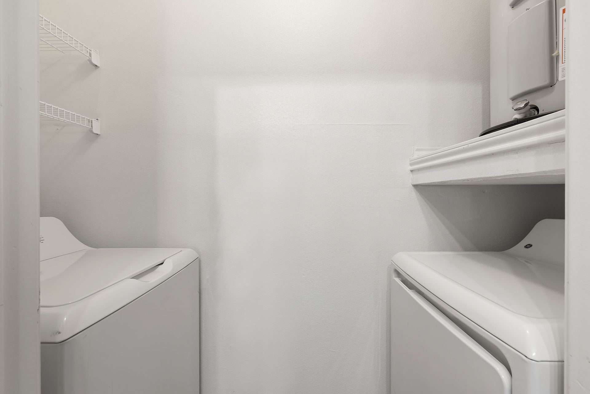 Laundry room with two white appliances and shelves in a narrow, bright alcove at Marquis at Bellaire Ranch in Fort Worth, TX