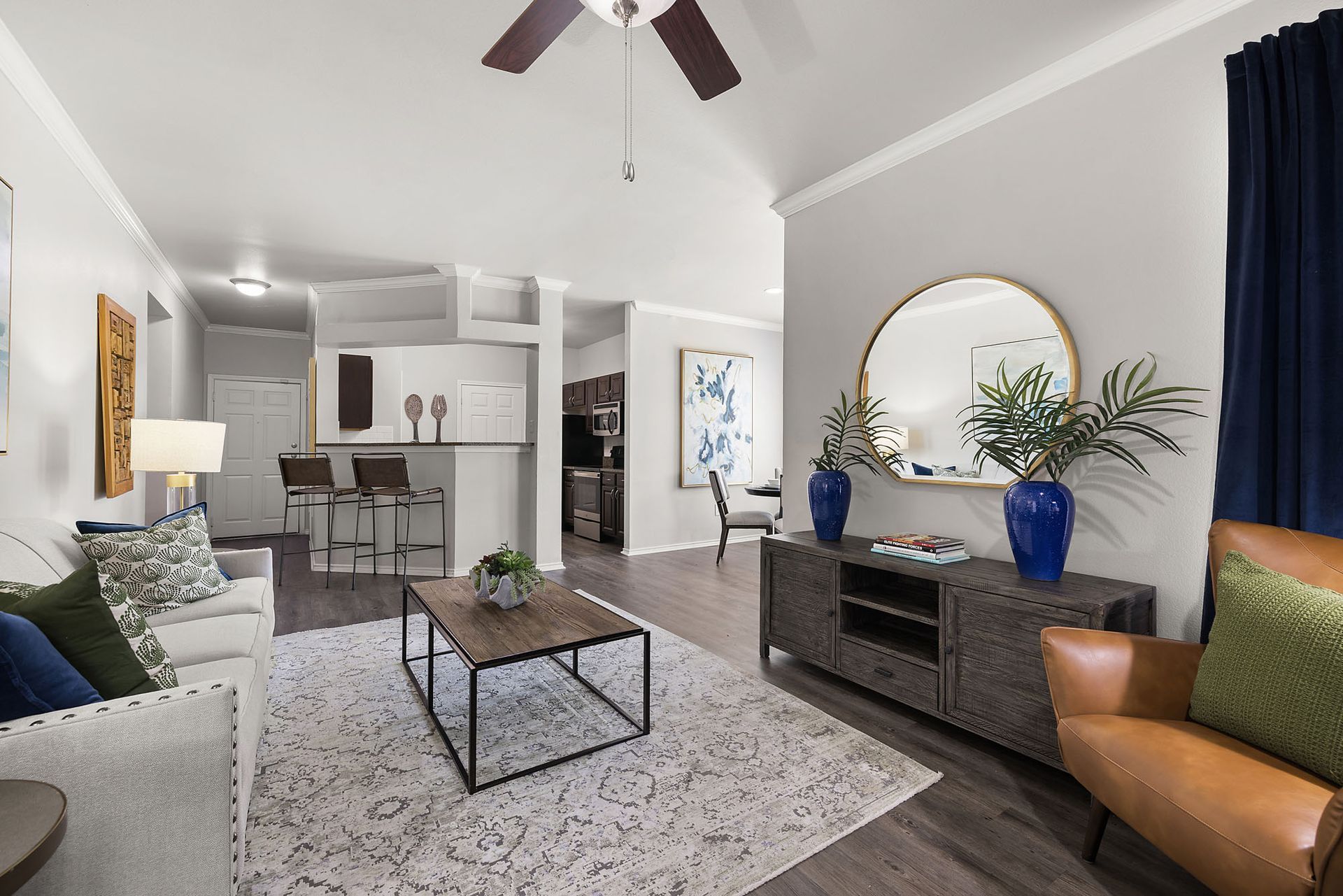 Bright living room with gray sofa, tan chair, glass coffee table, and kitchen bar in the background at Marquis at Bellaire Ranch in Fort Worth, TX