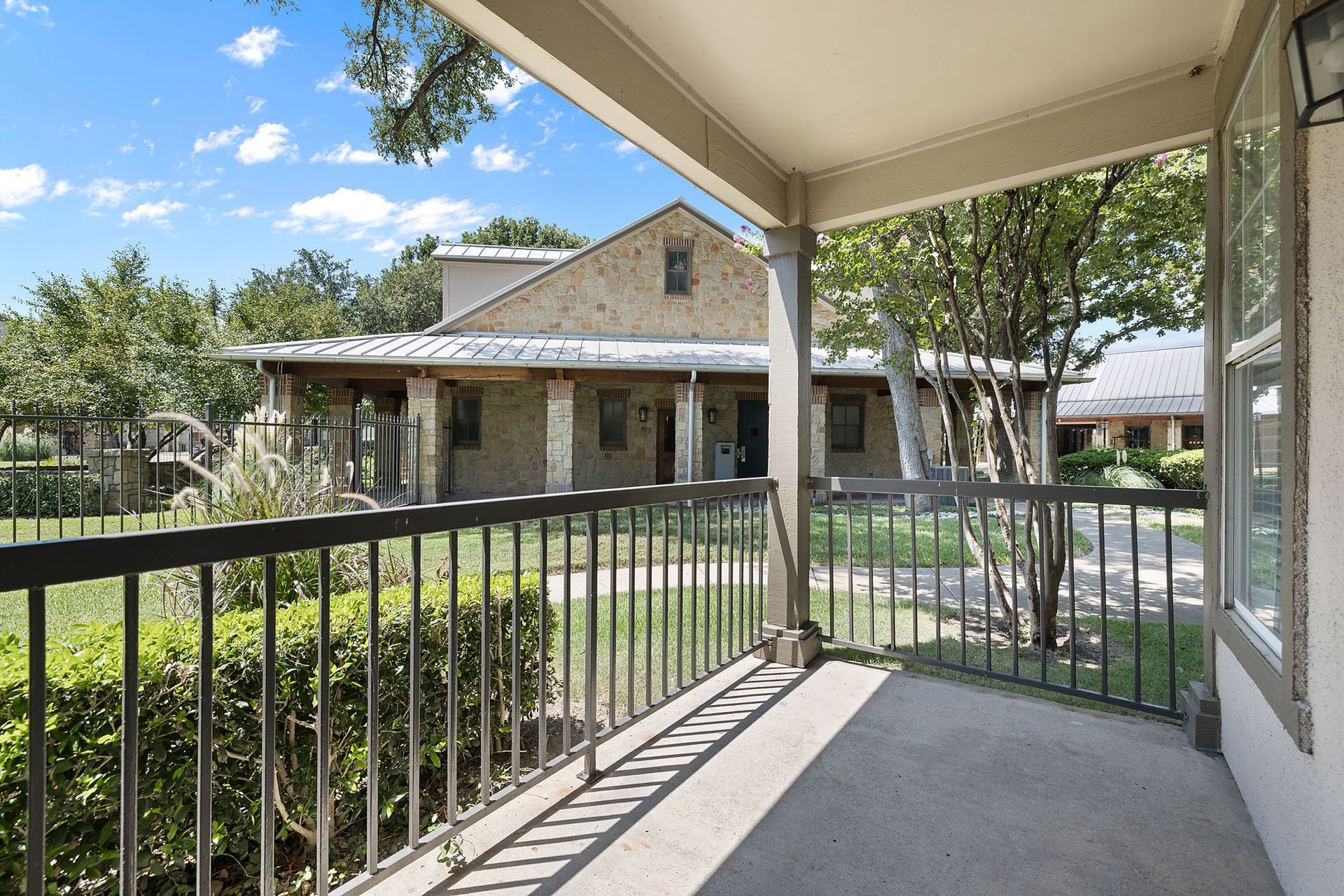 Covered porch overlooking a stone house, with black railings, shrubs, and a sunny yard at Marquis at Bellaire Ranch in Fort Worth, TX.