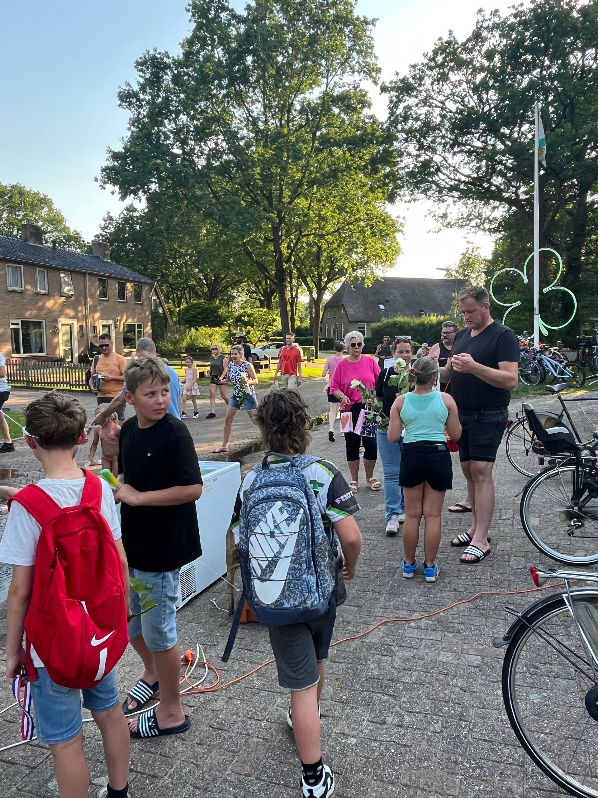 Kinderen met rugzakken verzamelden zich buiten bij fietsen op een schoolplein of in een park, met volwassenen in de buurt.