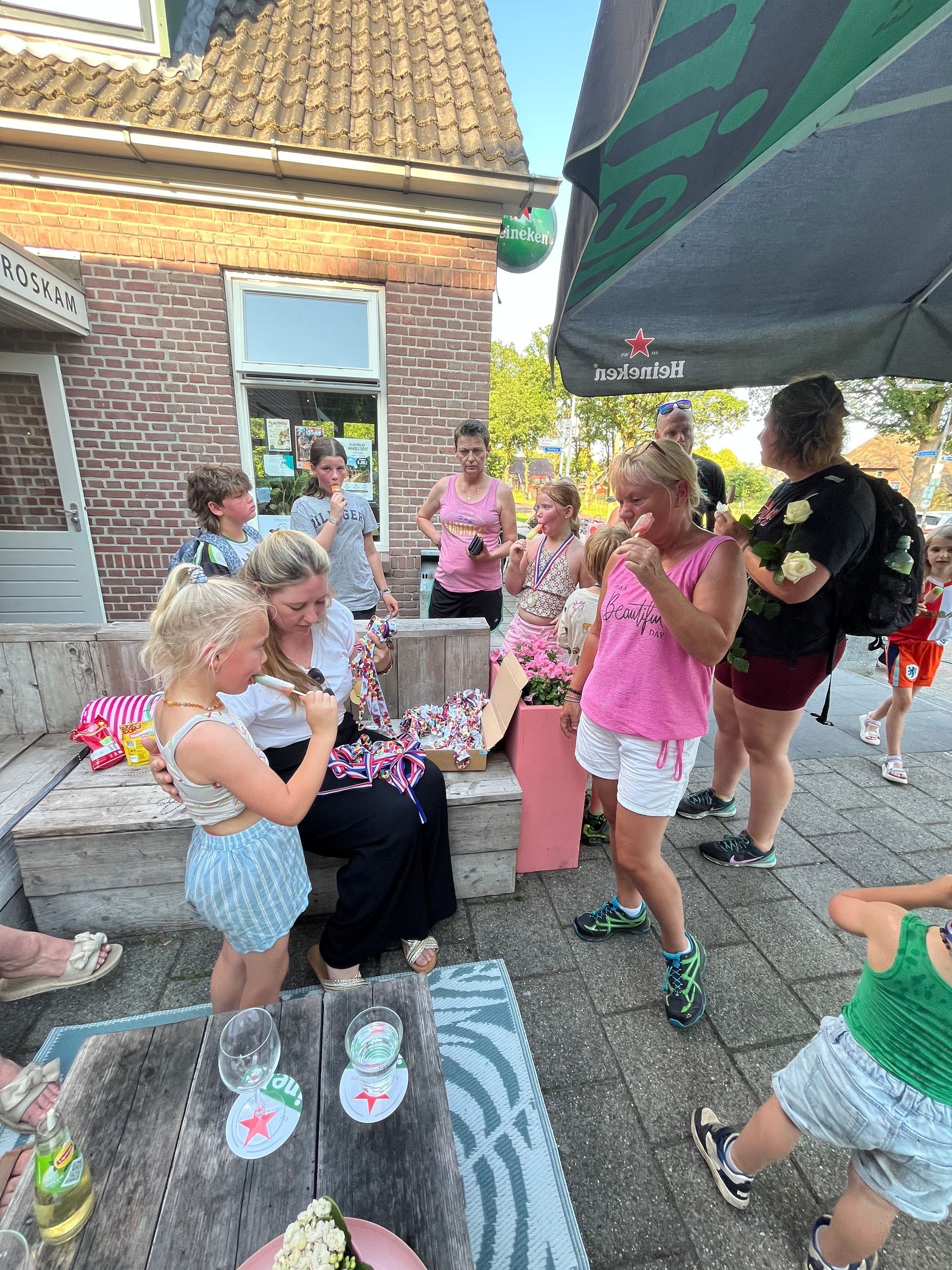 Kinderen in kleurrijke outfits verzamelen zich buiten rond een bankje met drankjes en lekkernijen tijdens een huisfeestje.