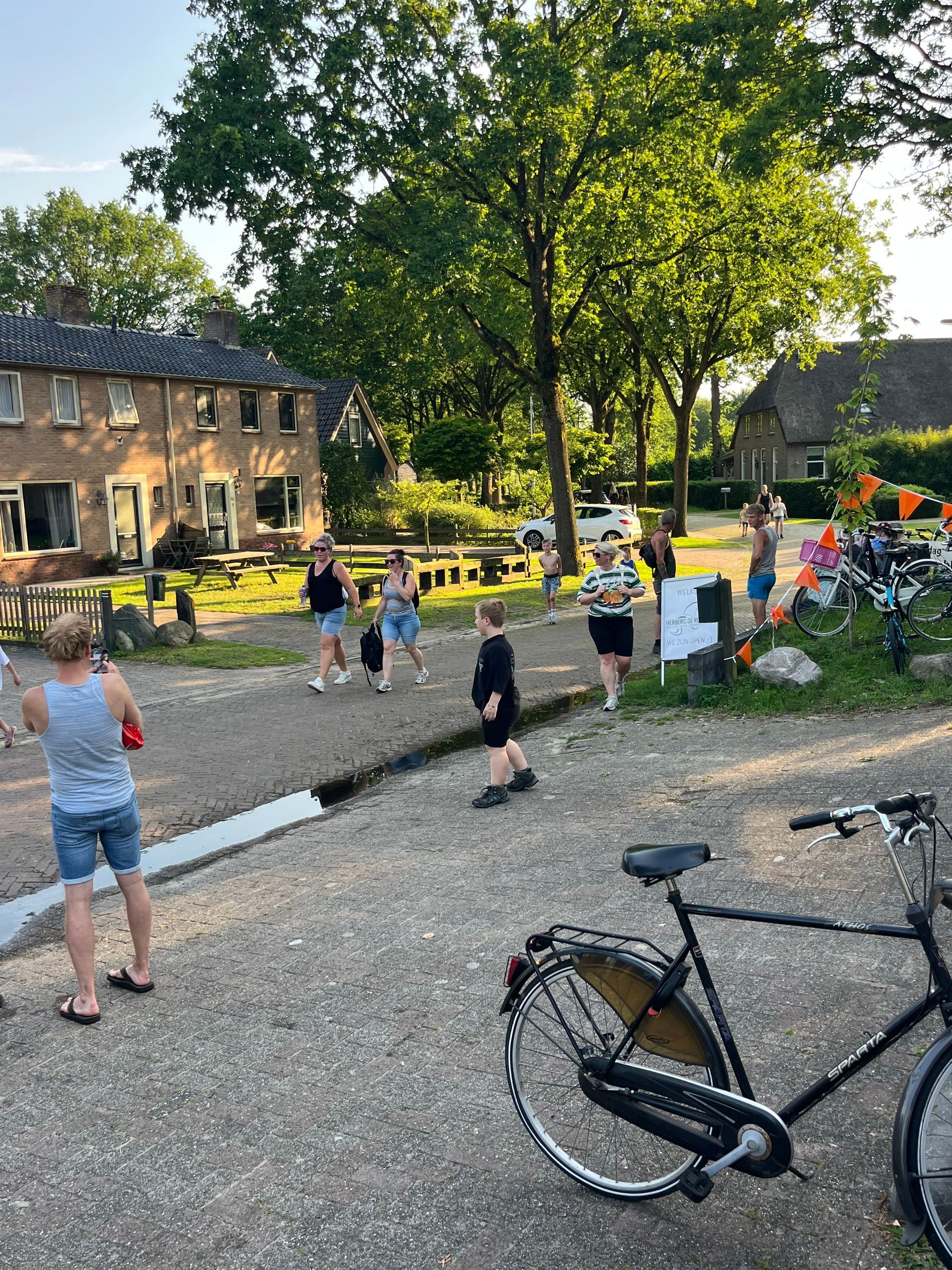 Mensen wandelen in een zonnige binnentuin naast stenen gebouwen, met fietsen op de voorgrond.
